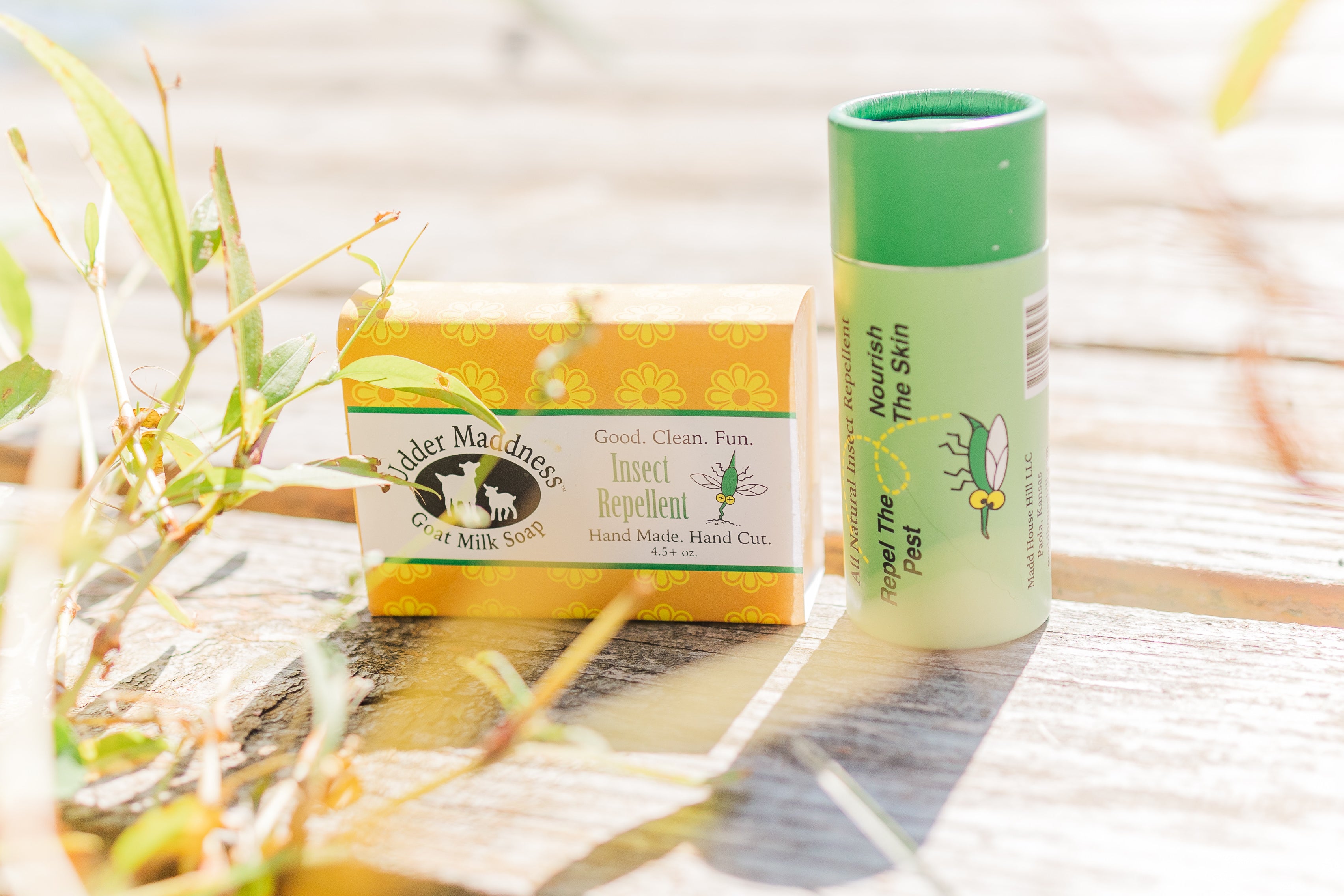 Madd House Hill Udder Maddness All Natural Insect Repellent Lotion Stick and Goat Milk Soap displayed outdoors on wood surface with natural foliage